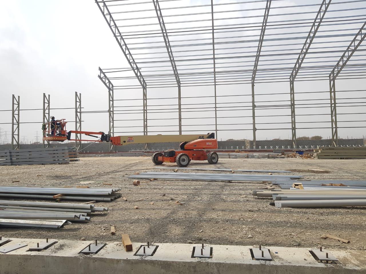 Stacked steel beams and cut sections arranged for fabrication in a busy metal workshop
