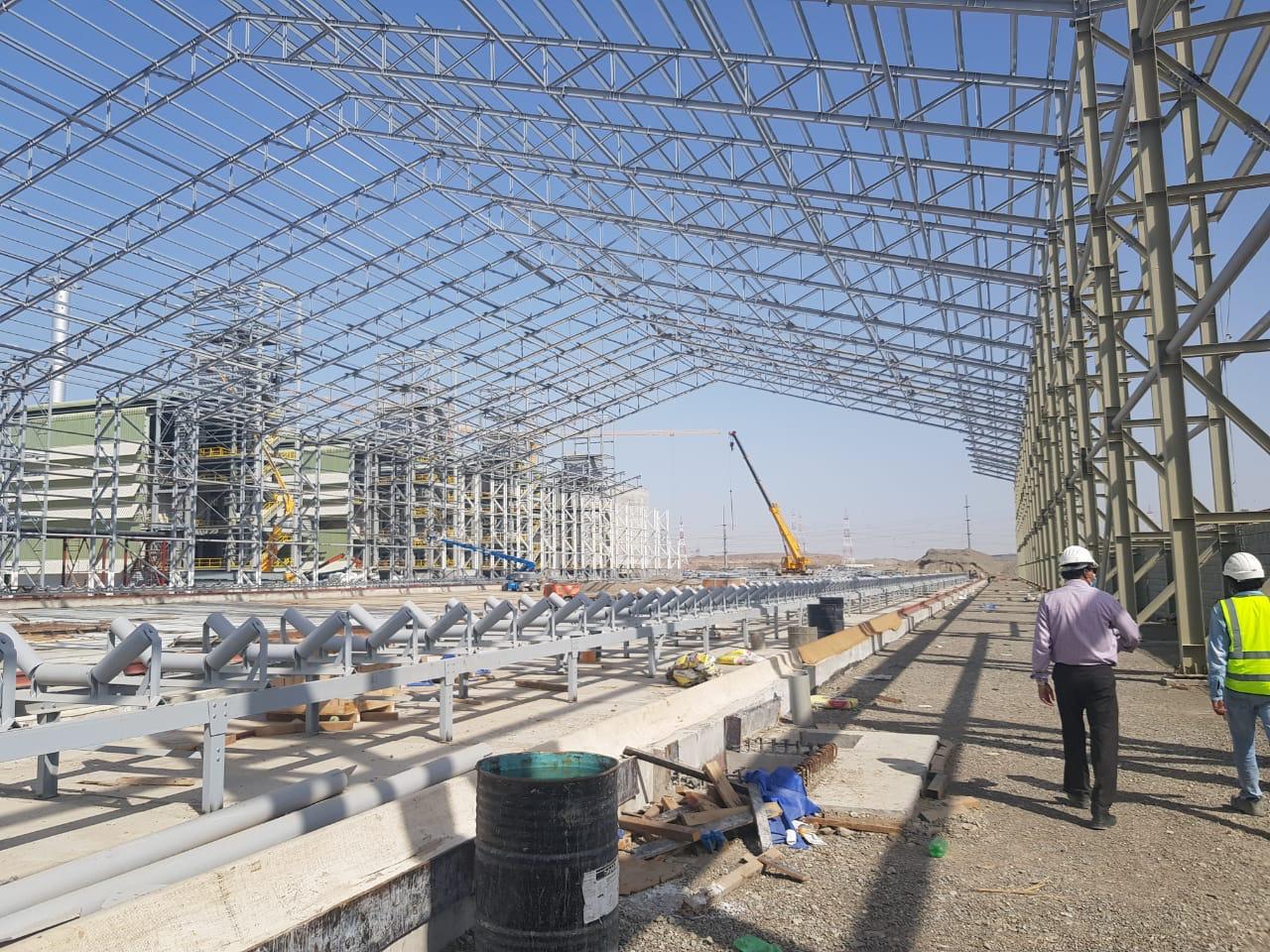 Large steel frame being positioned by workers inside a fabrication shop with an industrious atmosphere