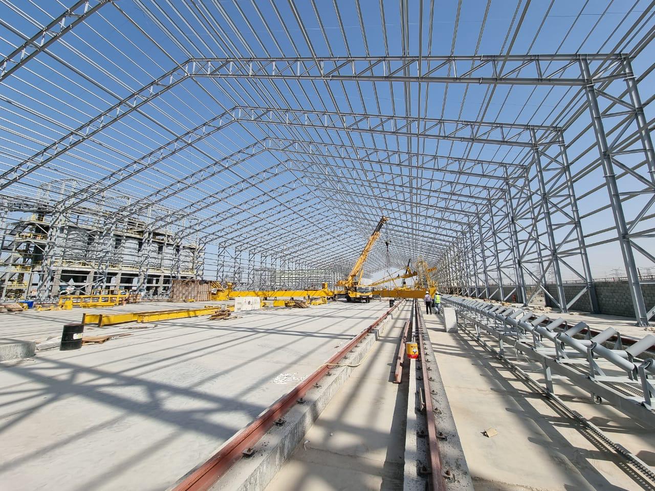 Fabricated steel panels stacked in a workshop beside scaffolding and tools in a practical worksite scene